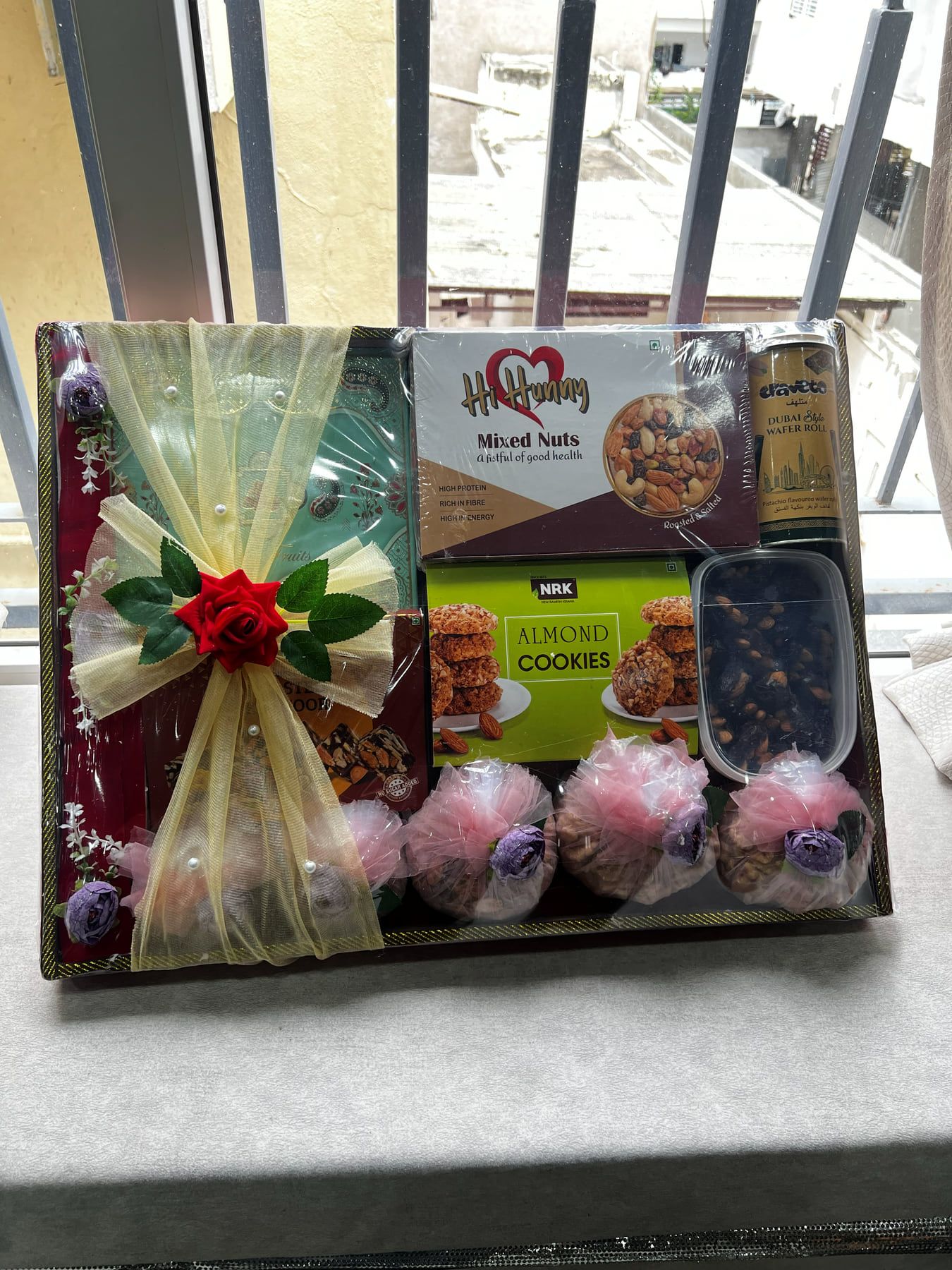 Gift tray with mixed nuts, almonds, cookies and pink pom-pom flowers under a cream tulle bow