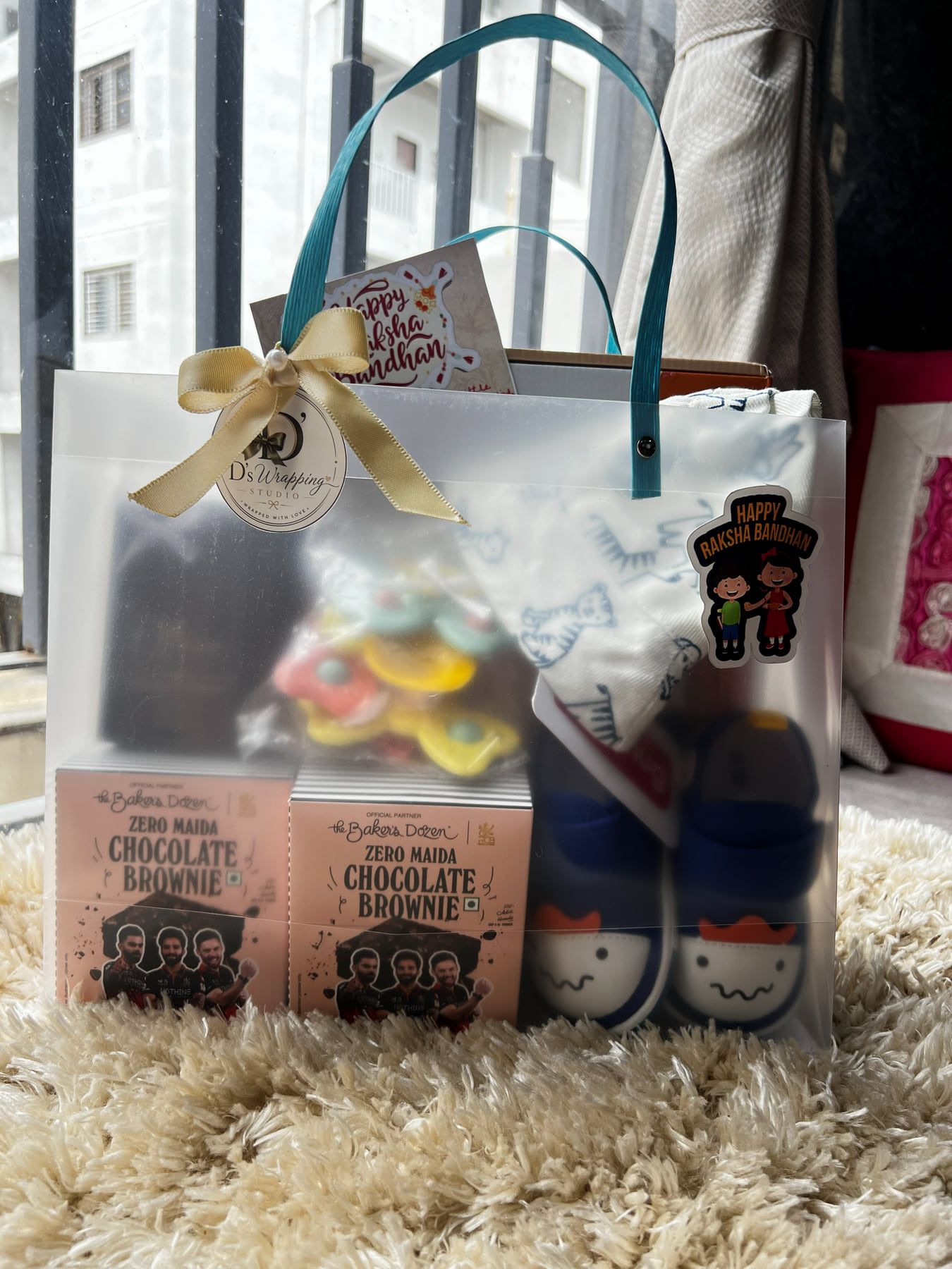 Clear gift bag with gold satin bow holding baby socks, chocolate brownies and treats with a Dwraps tag