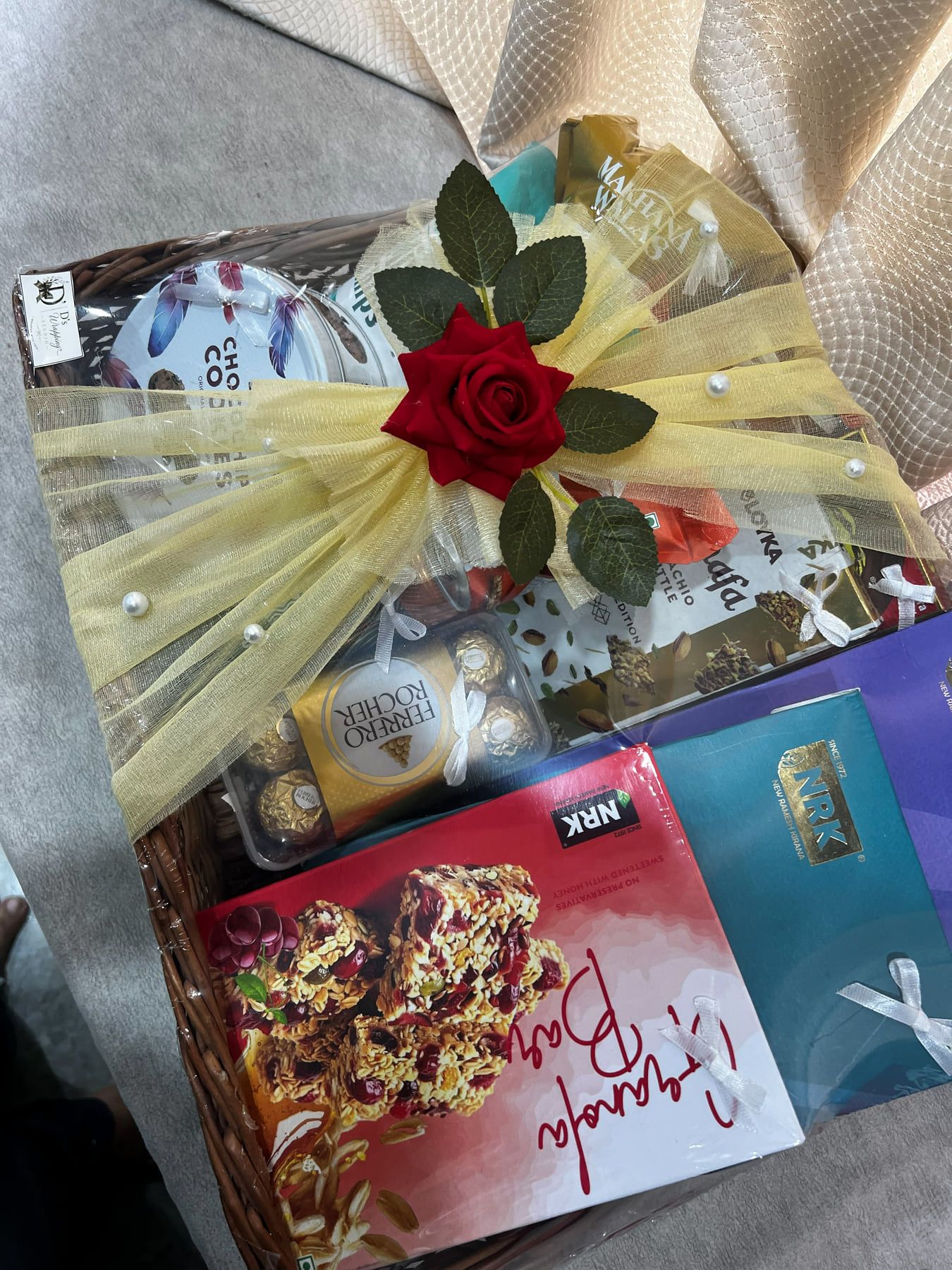 Wicker basket hamper wrapped in cream tulle with pearls and a red rose, filled with chocolates