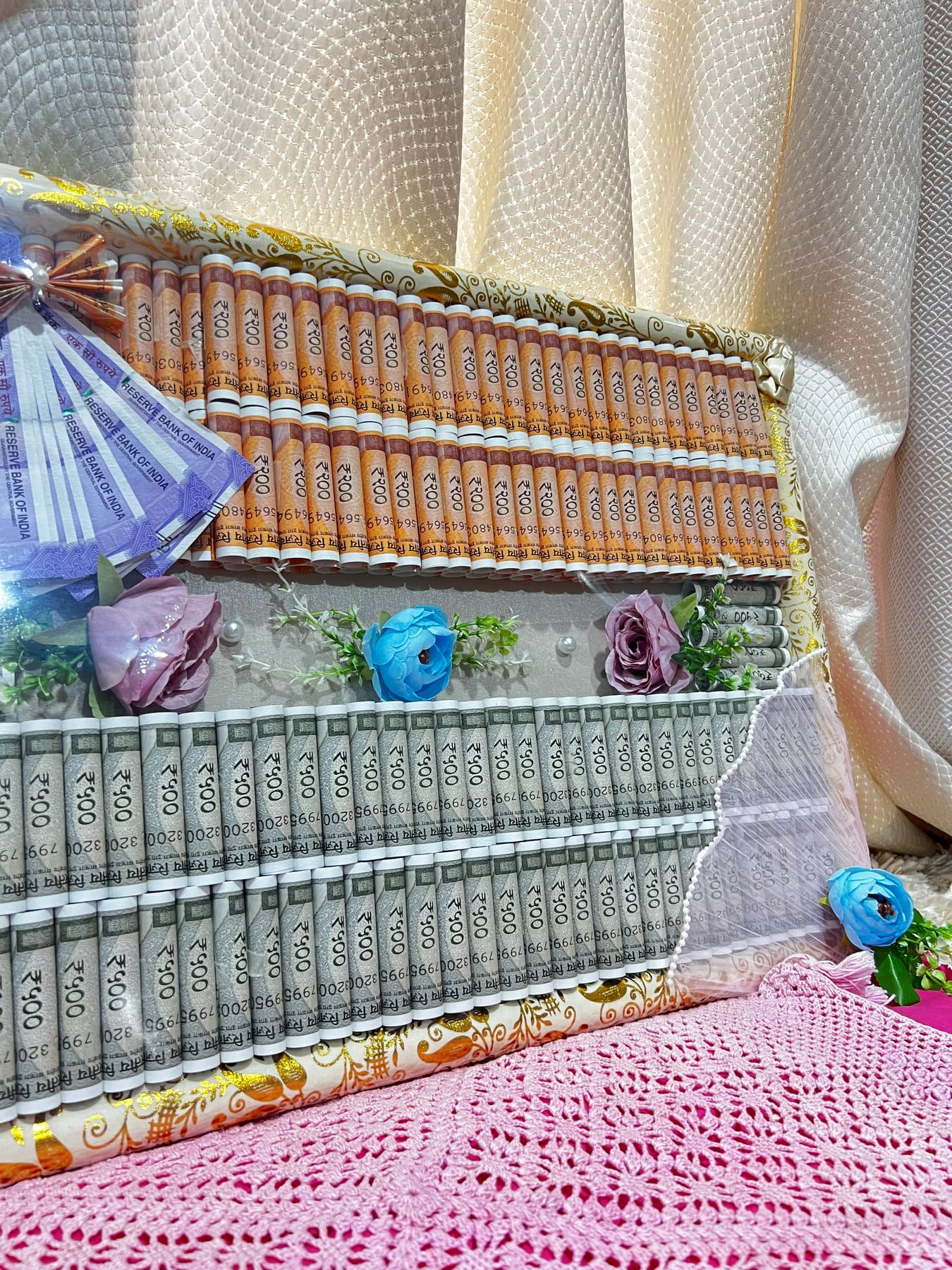 Rows of currency notes arranged on a lace-trimmed board decorated with fabric flowers
